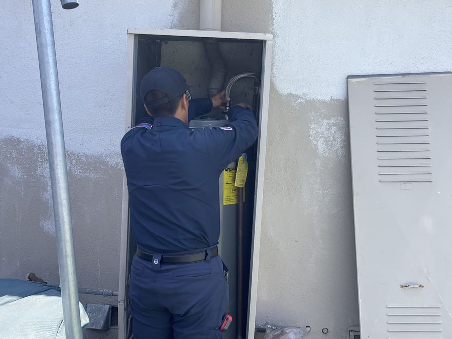 Drain & Plumbing Pros technician servicing a water heater in an exterior enclosure
