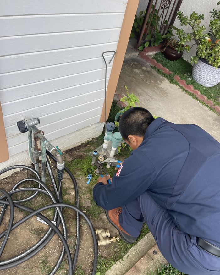 Plumber repairing an outdoor water line beside a house