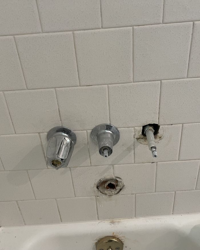 Tub and shower valve trim being replaced in a white tiled bathroom